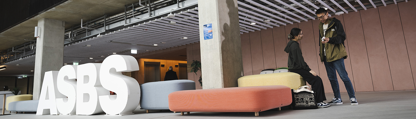 Two people walk through the lobby of the ASBS PG hub. Large white letters spell out ASBS.