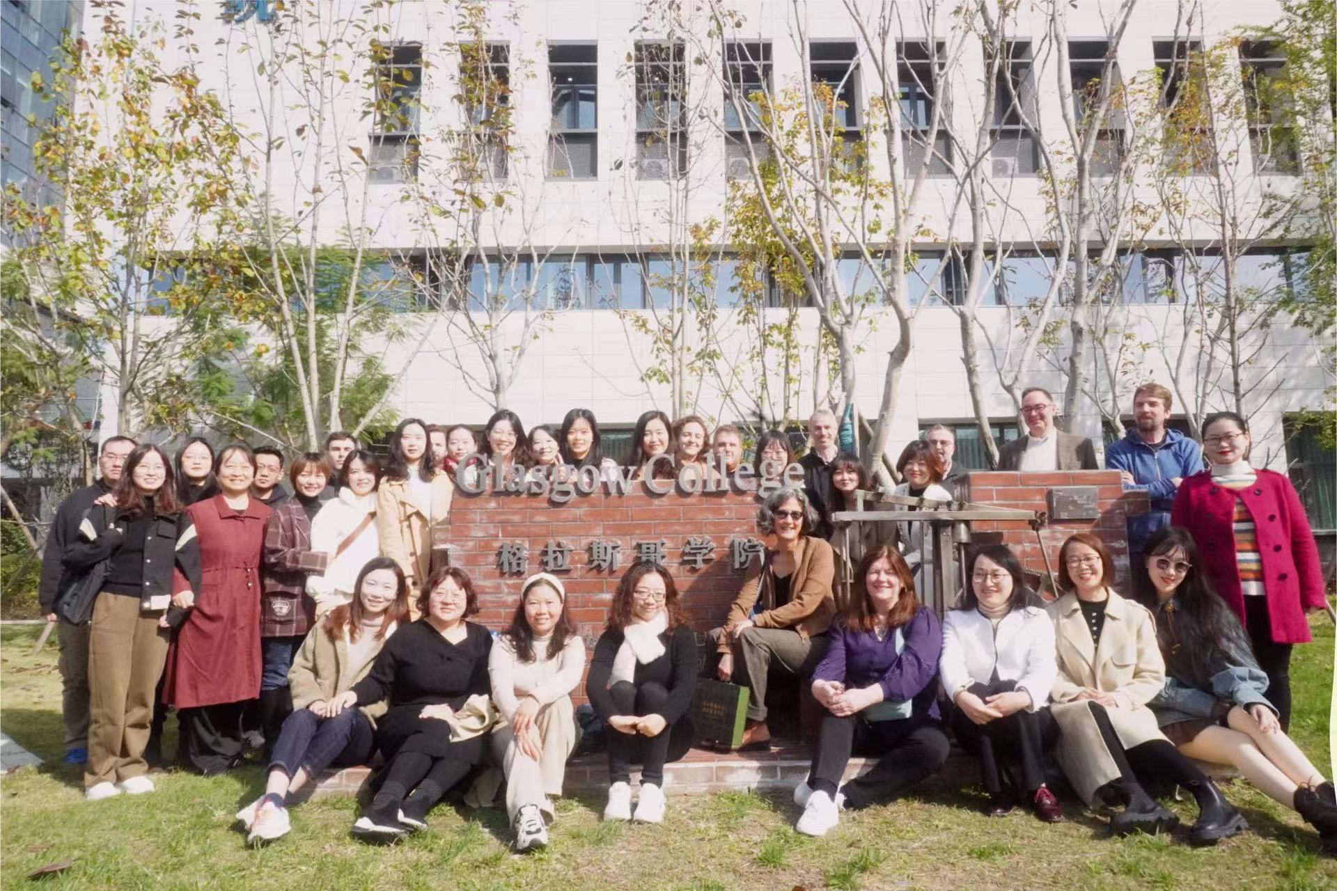 Group of teachers sit on the grass outside Glasgow College, UESTC during Professional Development week for English language teaching staff