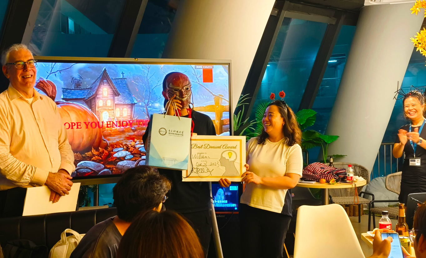 A student on stage in a Halloween horror mask being given his prize certificate by staff