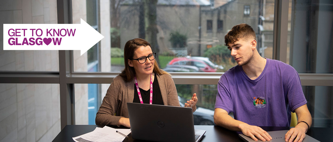 student and staff member chatting next to a laptop