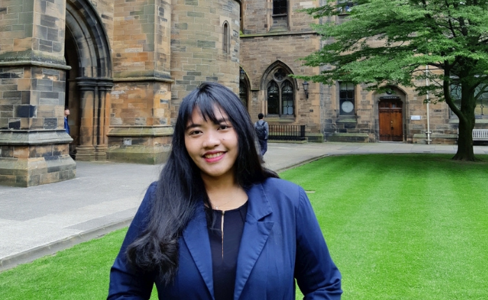A student in a dark blue blazer standing in the courtyard of the University of Glasgow