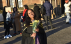 A woman stands in the UofG courtyard in a graduation gown, smiling and holding flowers