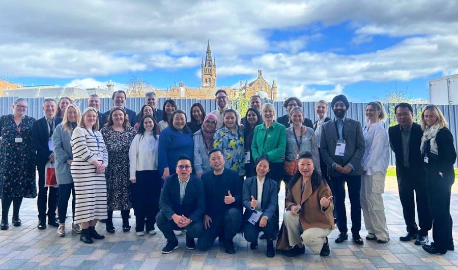 Attendees of the Stakeholder Summit posing in a group outside in the sunshine, with the Gilbert Scott Building tower in the background