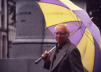 Dr Koff  with large umbrella in Glasgow next to statue in George Square