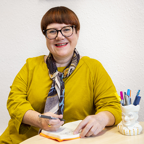 Professor Louise Welsh sitting at a table with a notebook and pens