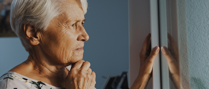 Photo of older woman standing at window during lockdown