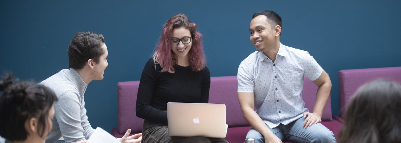 Group of students around a laptop chatting and studying