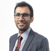 Profile picture of Imran Ahmad.  He is wearing a grey suit with a red and black tie. He has glasses and is smiling directly at the viewer.