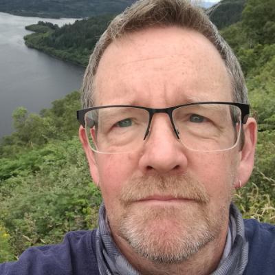 A man with glasses looking at camera above a lake