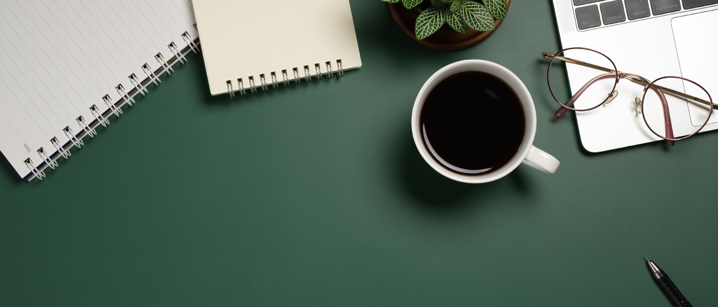 Photo of a desk with pen, notepads and a cup of coffee