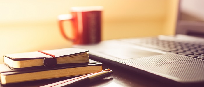 Photo of a desk with a cup of coffee, books and a laptop	